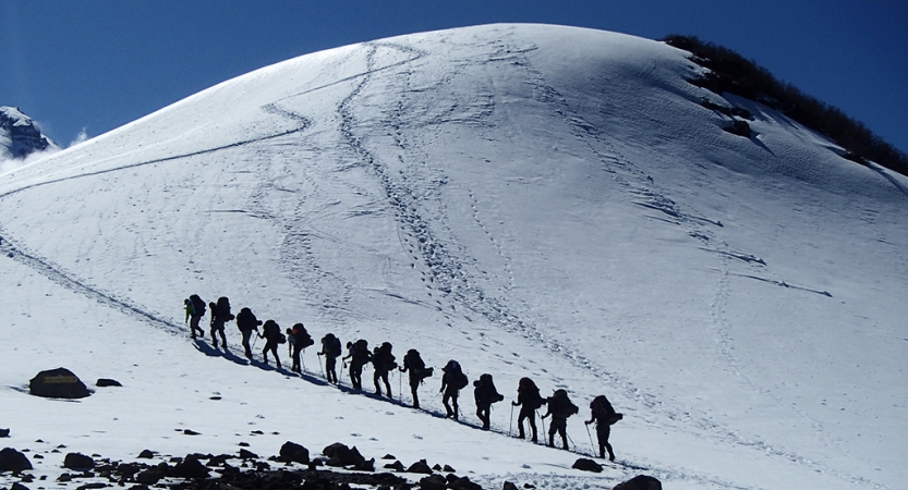A group of people wearing backpacks hike in a line up a snowy incline.